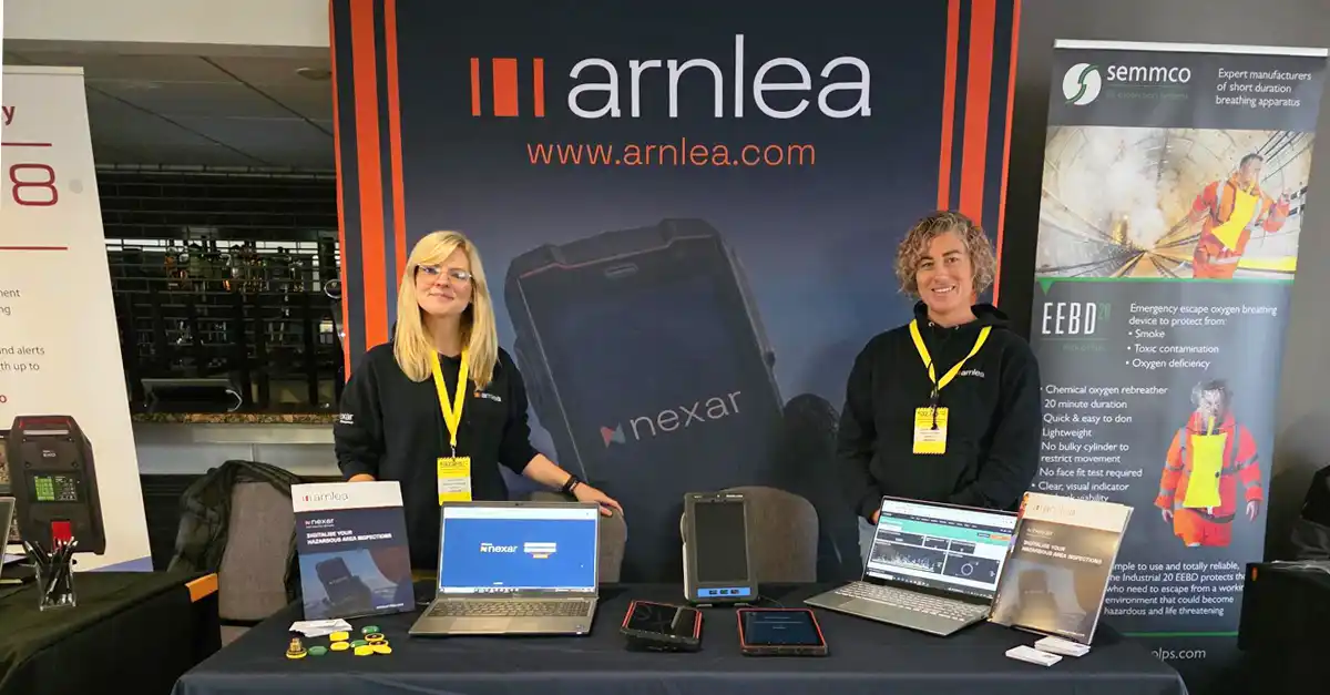 Arnlea Systems team members Claire Murray and Jen Hughes at the Hazardex exhibition in Ellesmere Port, standing at the Arnlea stand with Nexar Ex inspection software displayed on laptops and tablets.
