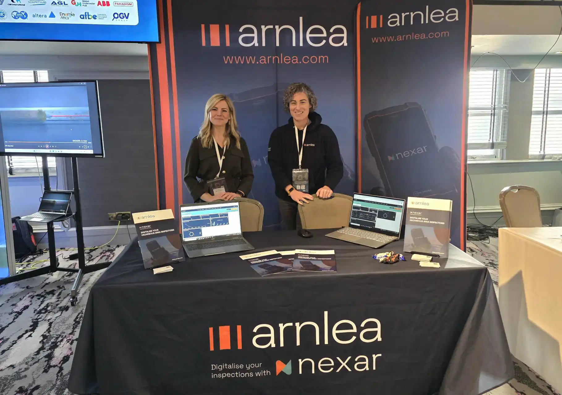 Claire Murray and Jen Hughes standing behind the Arnlea exhibition stand with Nexar software displays at the Wider African Energy Summit 2025 in Aberdeen.