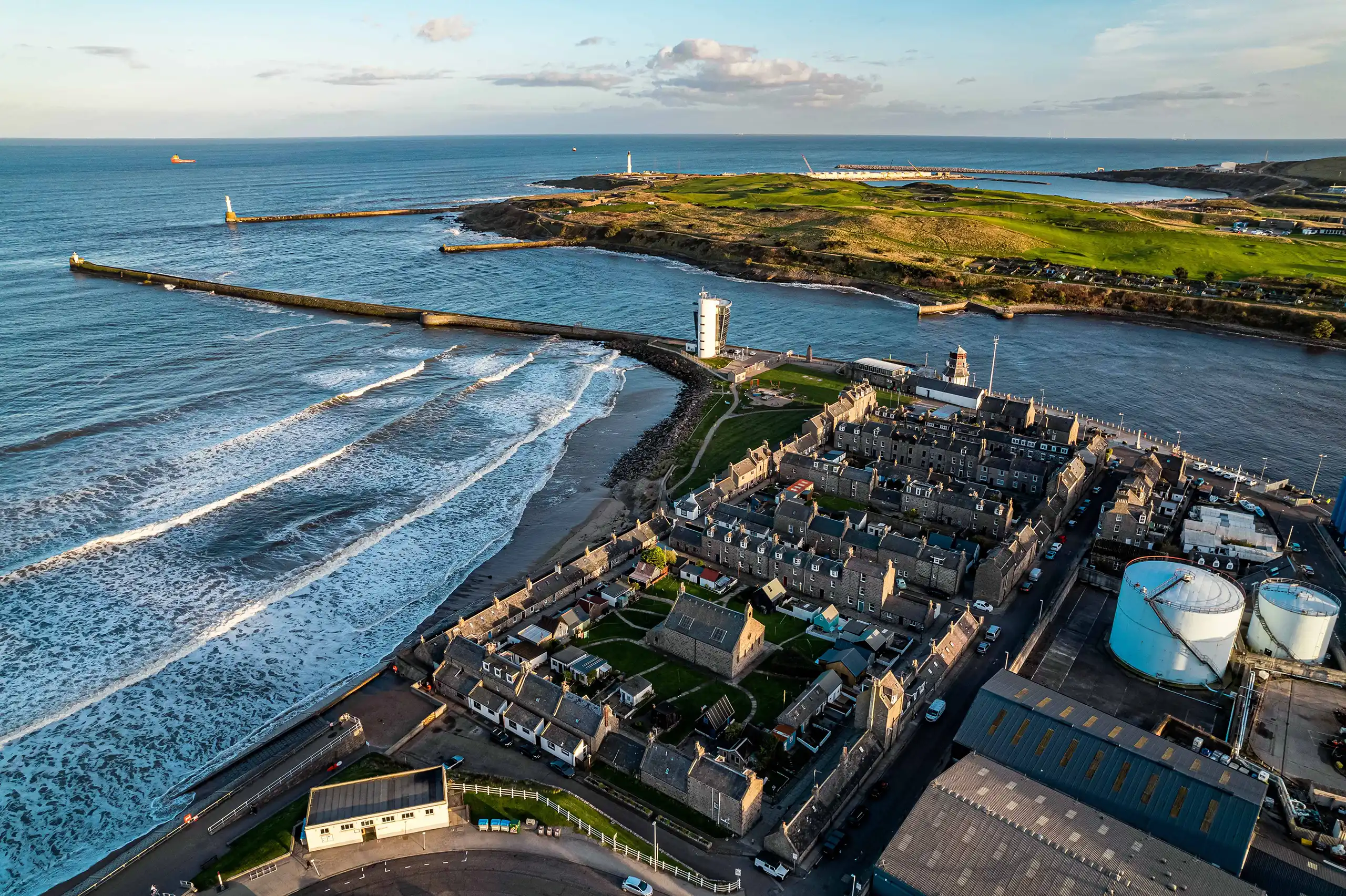 Aerial view of Aberdeen coastline showing the harbour, river mouth, residential streets, and industrial energy infrastructure along the shoreline.