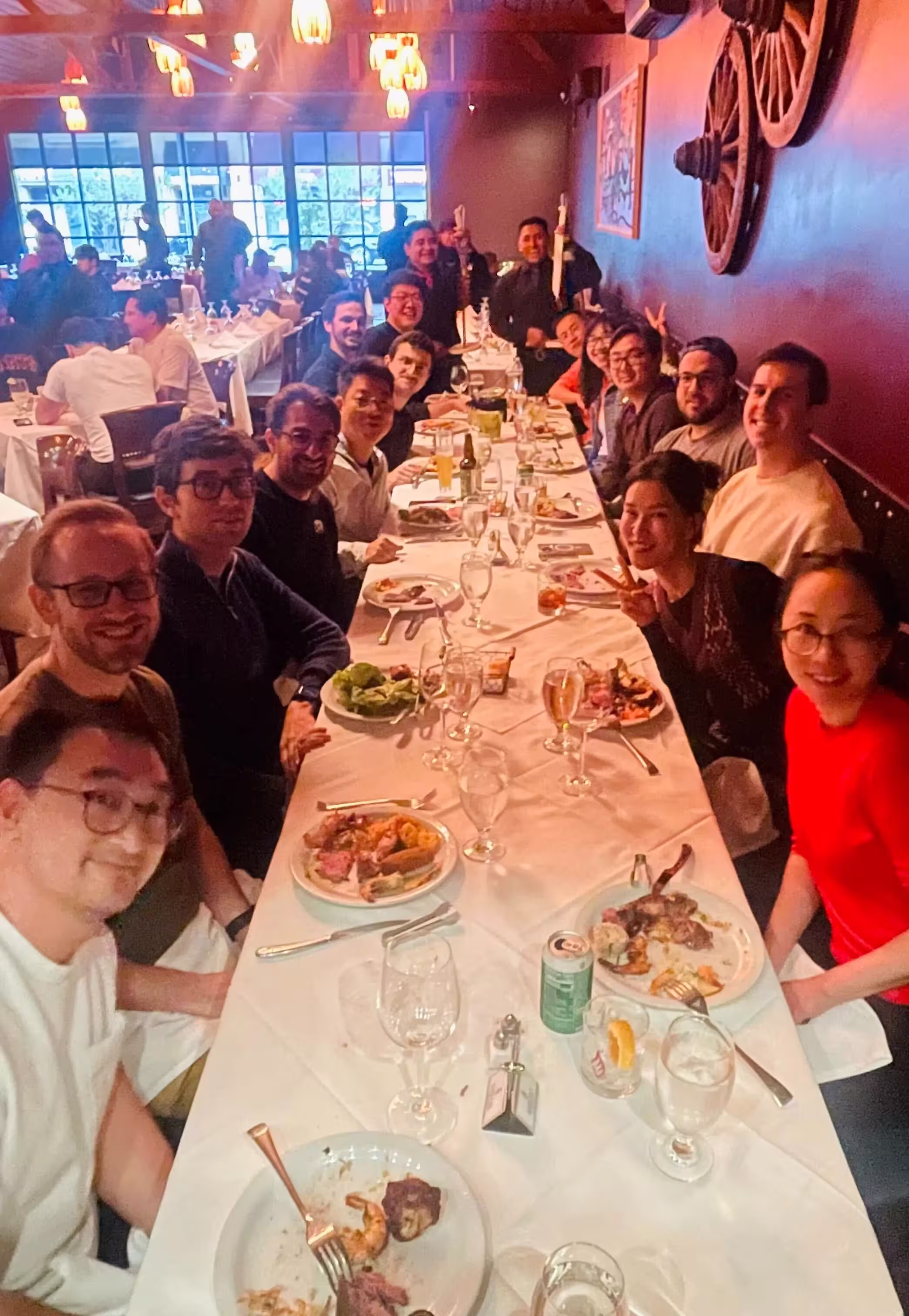 A large group of people seated around a long restaurant table enjoying a meal together, smiling and posing for the photo.