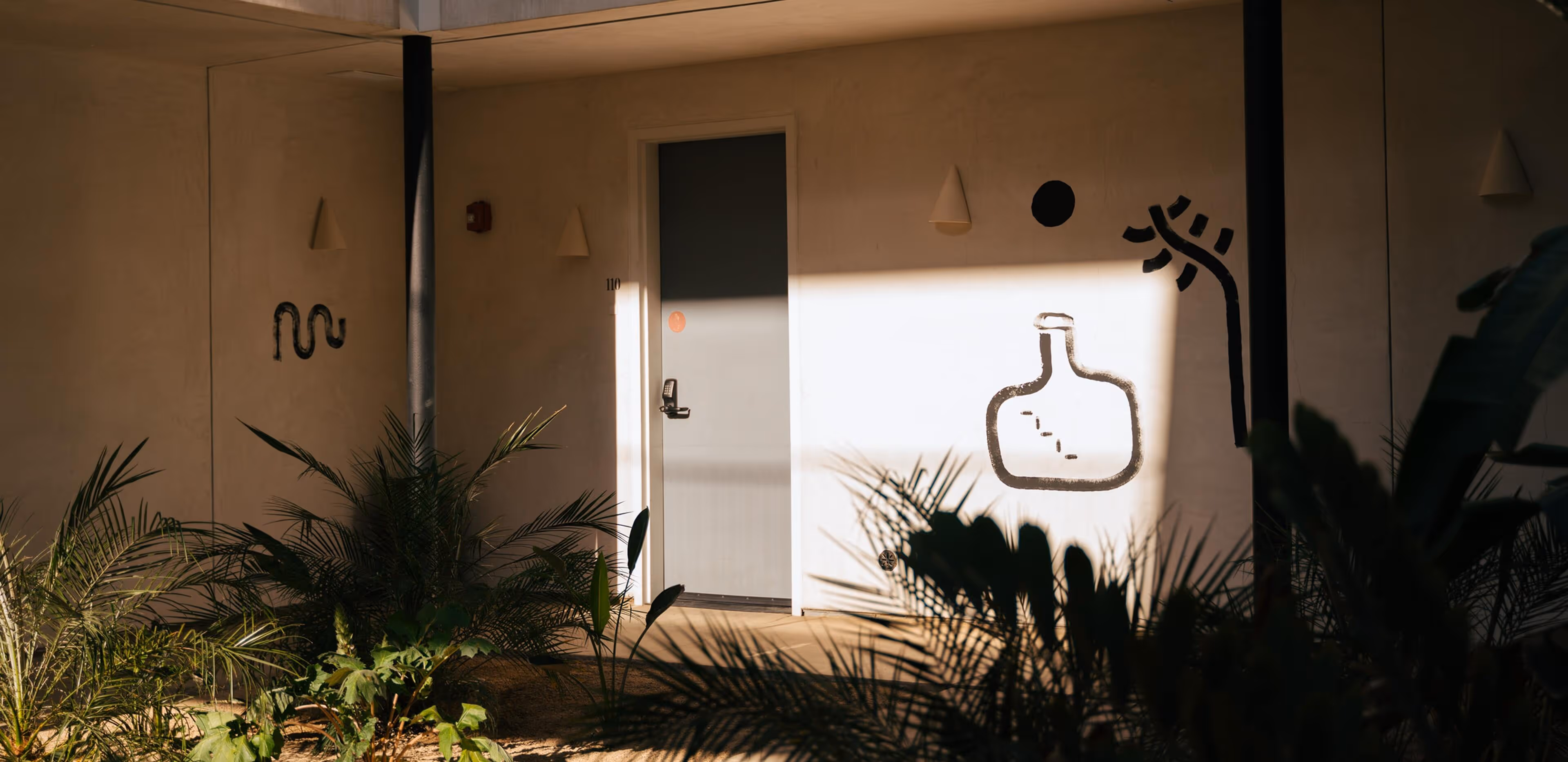 Minimalist hotel corridor with pale blue door #110, surrounded by potted palms and abstract black wall art, bathed in warm sunlight and shadow.