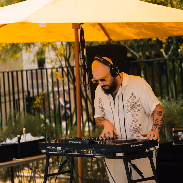 DJ performing live music outdoors under a yellow umbrella at a summer event.