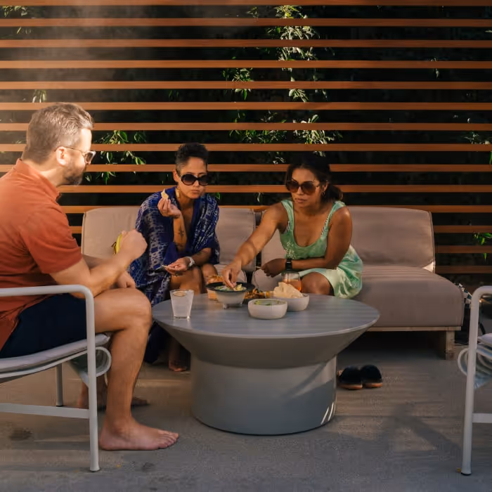 Group of friends enjoying snacks and drinks outdoors on a sunny patio lounge.