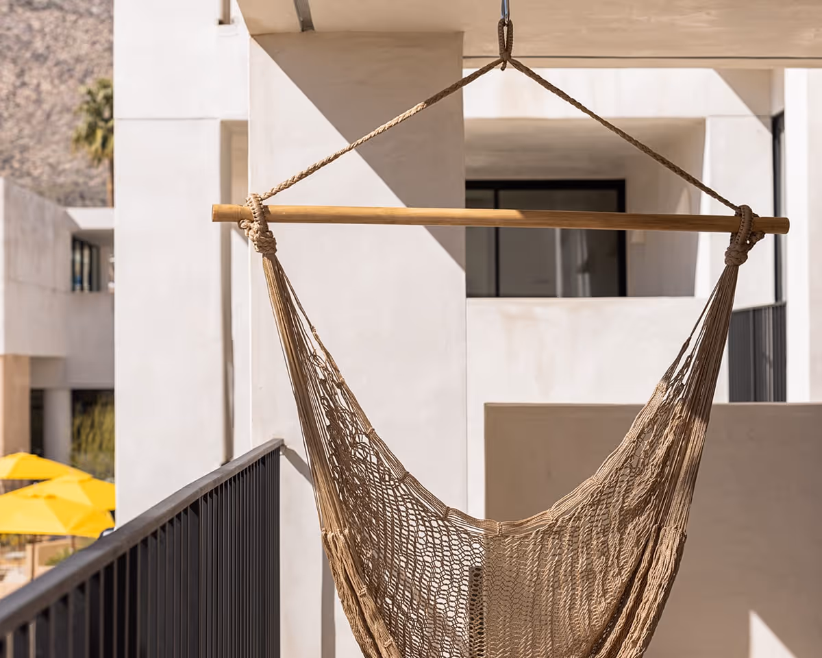 Balcony hammock hanging outside a modern suite with mountain views and yellow pool umbrellas below.