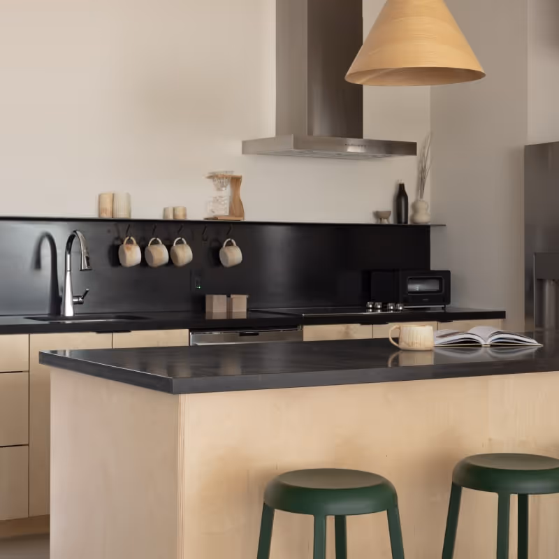 Contemporary kitchen with black countertops, wooden island, and green bar stools under a cone-shaped pendant light.