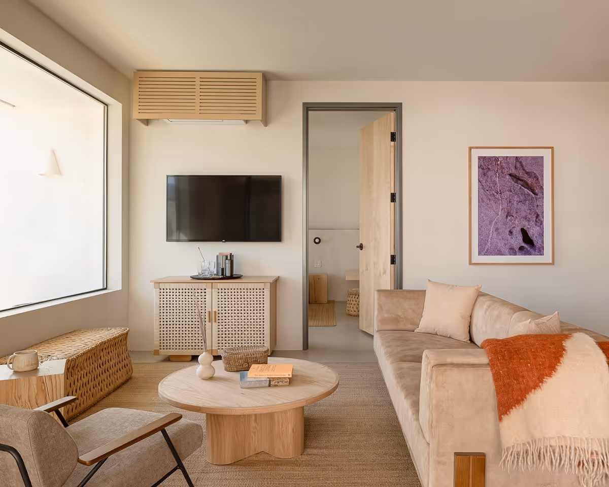 Modern living room with beige sofa, round wooden coffee table, and wall-mounted TV in a minimalist suite.