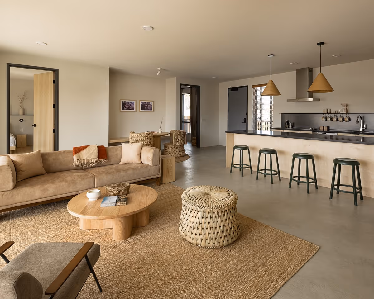 Spacious open-plan living room with beige sofa, woven ottoman, and modern kitchen island with bar stools.