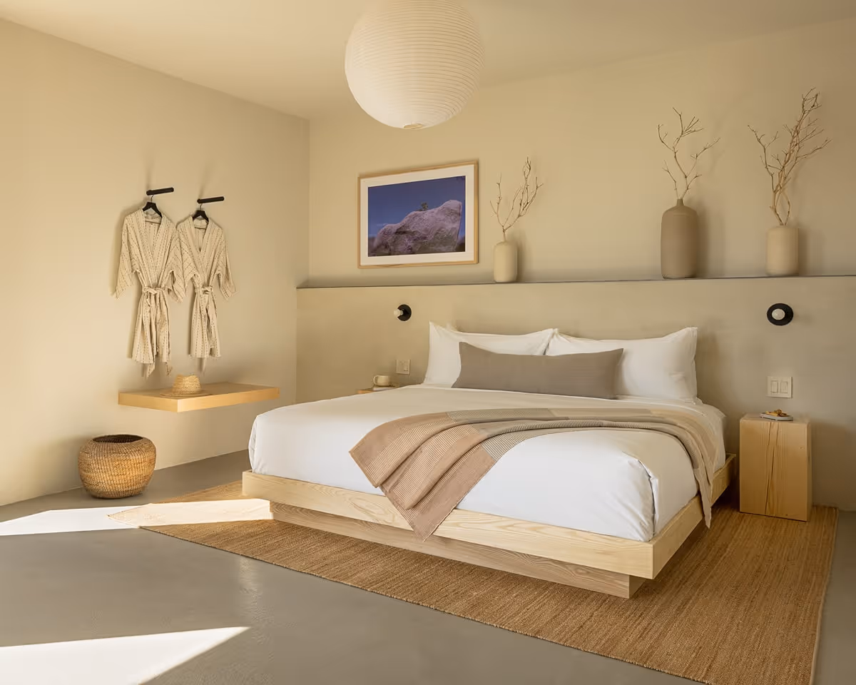 Minimalist bedroom with wooden platform bed, neutral linens, and decorative vases on a ledge above the headboard.