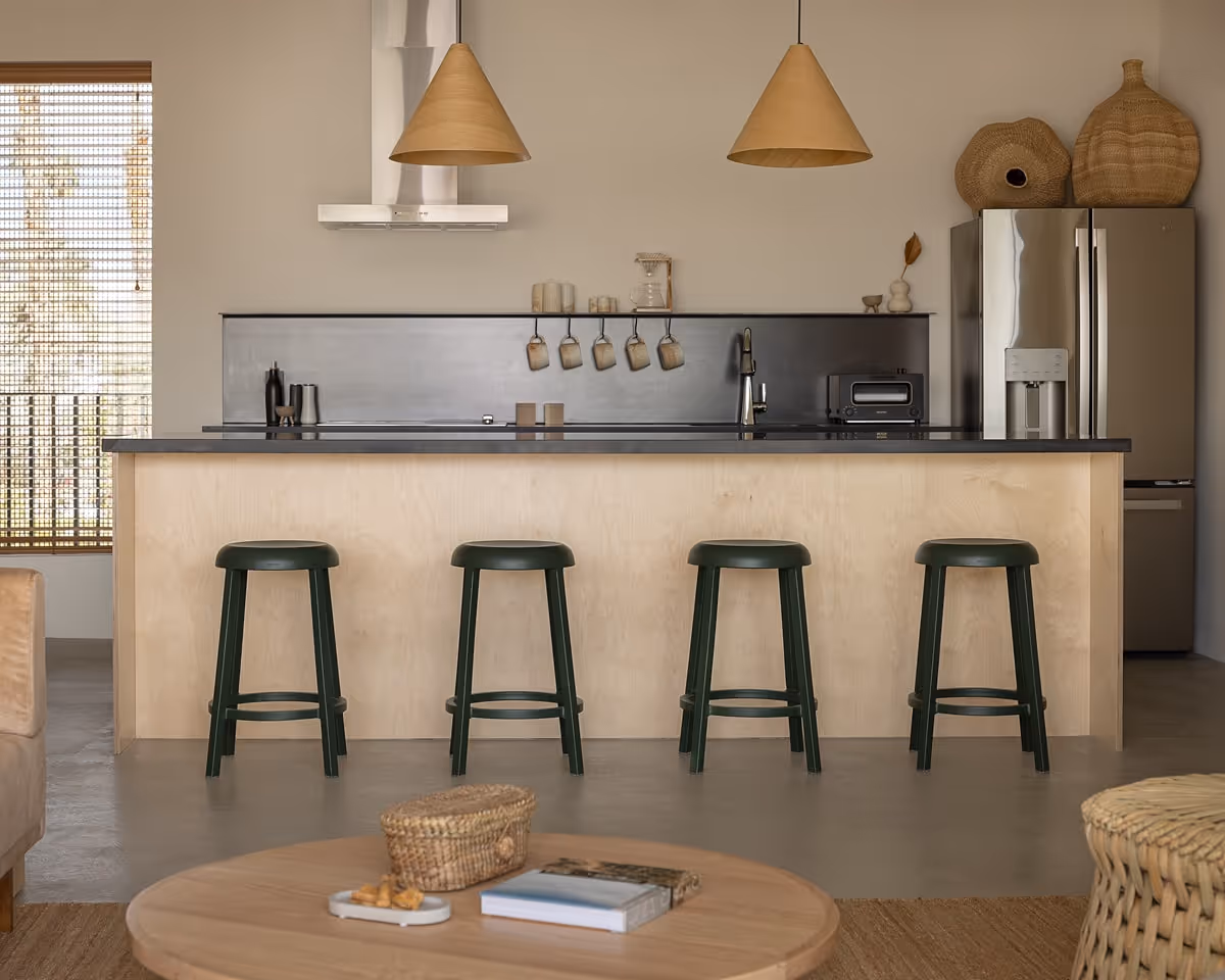 Modern kitchen with black countertops, light wood cabinetry, green bar stools, and natural woven decor accents.