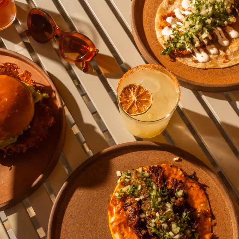 Hands holding white ceramic mug with matcha green tea latte featuring heart-shaped latte art, cozy teal sweater in sunlight