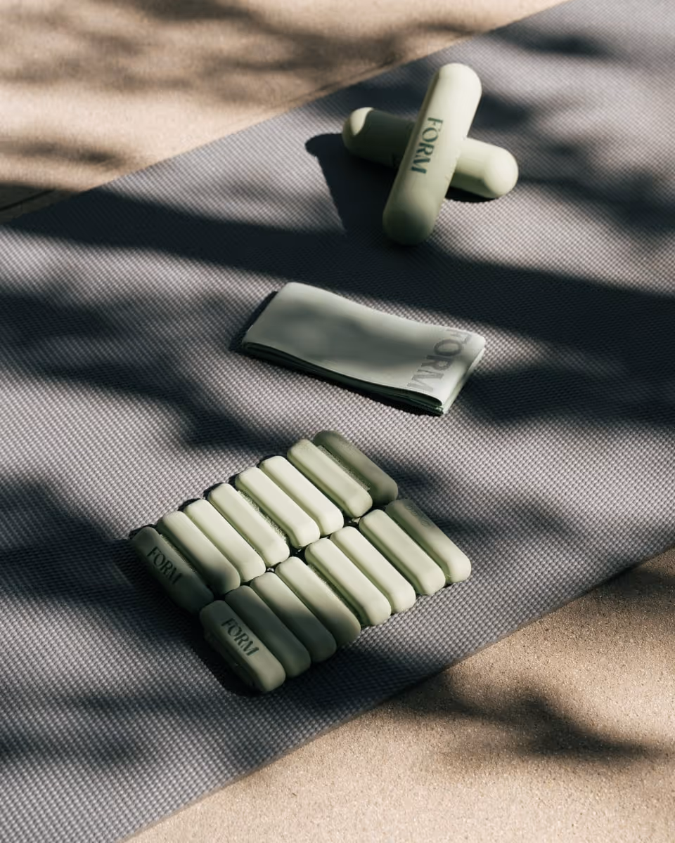 Modern fitness equipment from Form, including hand weights and resistance bands, neatly arranged on a yoga mat in a sunny outdoor setting.