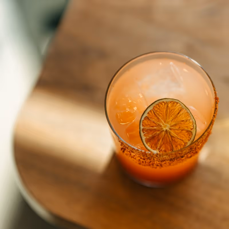 Refreshing orange cocktail with chili salt rim and dried lime garnish on a wooden table.