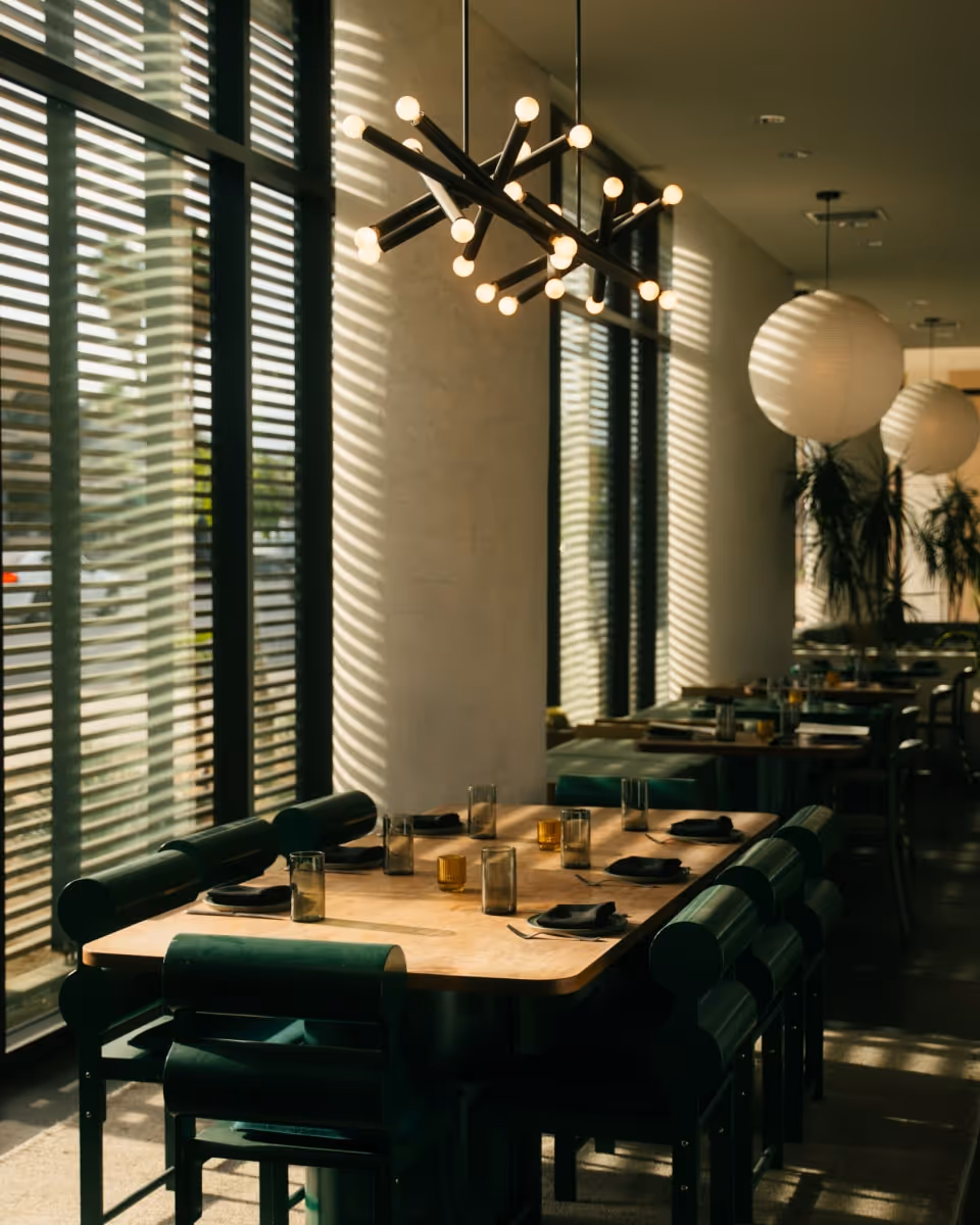 Modern restaurant dining area with natural light, stylish pendant lighting, and tables set with glasses and napkins.
