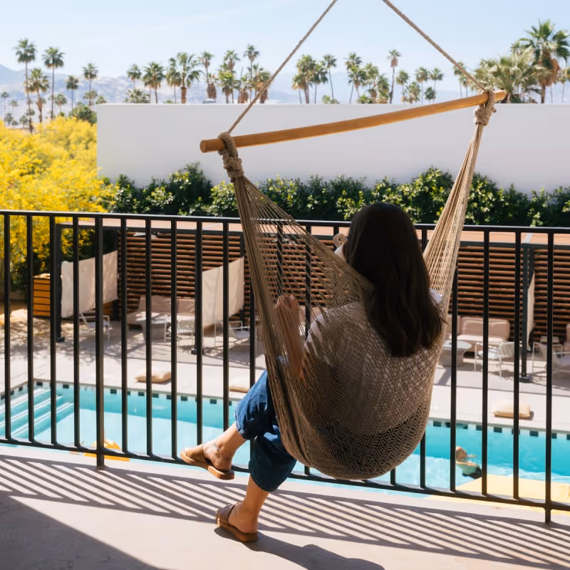 Guest relaxing on balcony hammock overlooking pool and palm trees at desert hotel