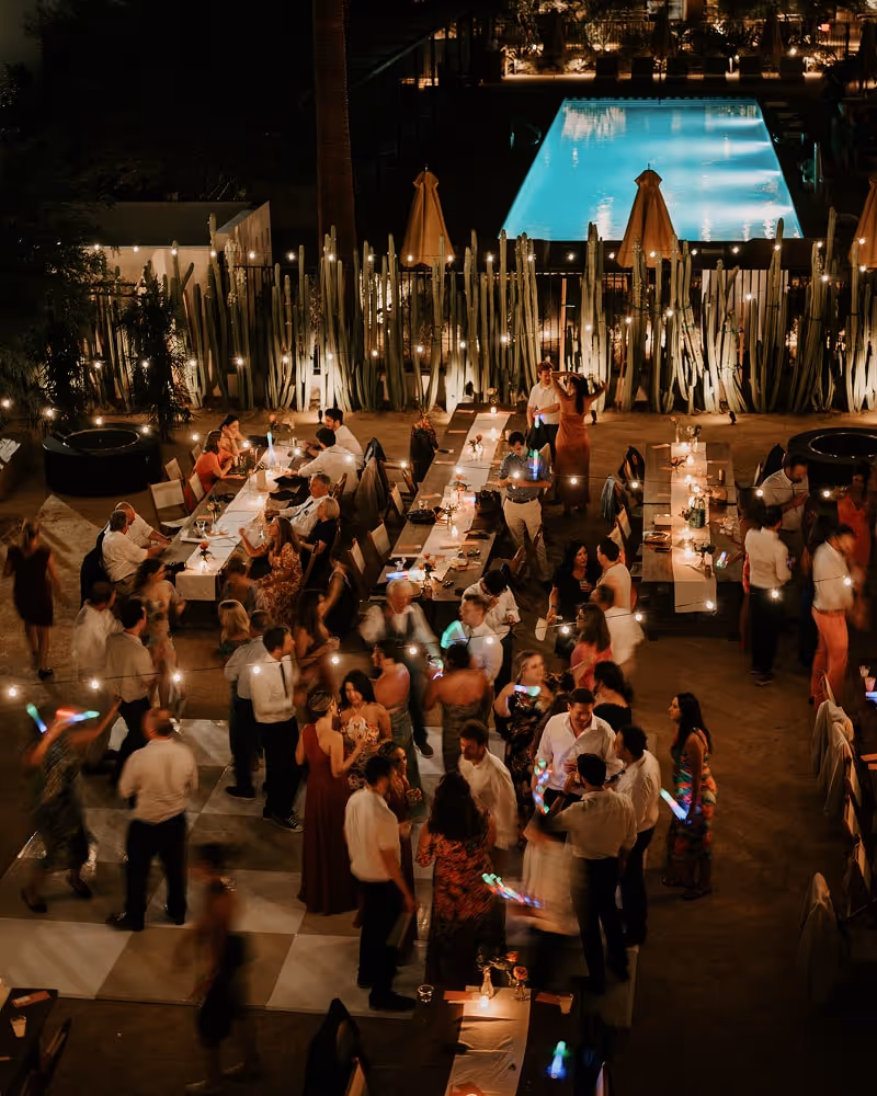 Evening wedding reception with guests dining and dancing around a pool under string lights and festive atmosphere