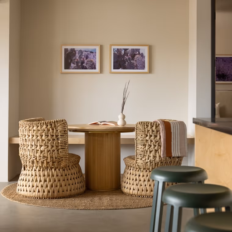 Cozy dining nook with woven chairs, round wooden table, and framed cactus artwork.