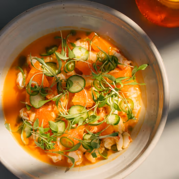 Fresh seafood dish with orange slices, cucumber, and microgreens in a light broth.