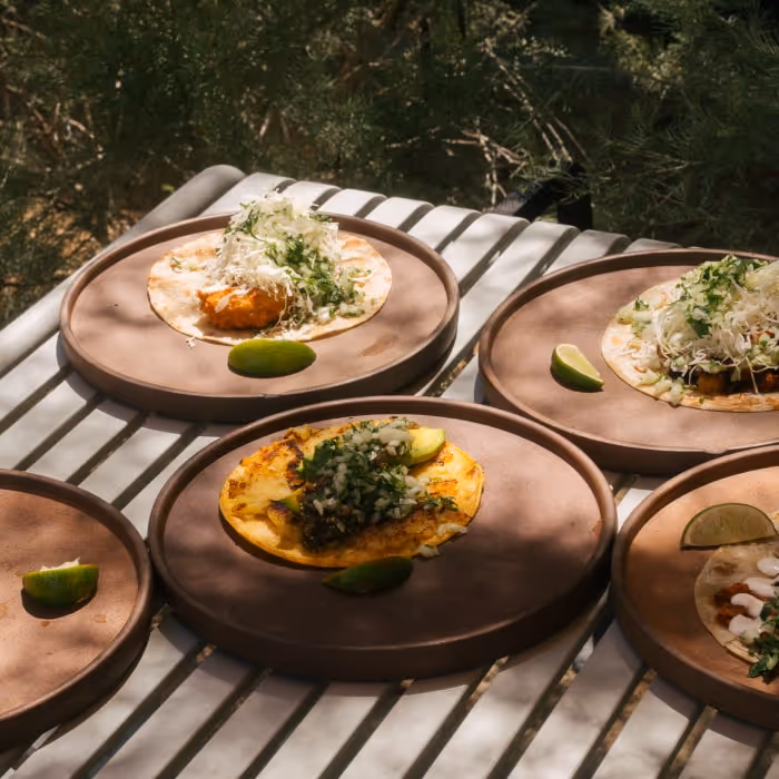 Assorted tacos with fresh toppings and lime wedges served on rustic brown plates.