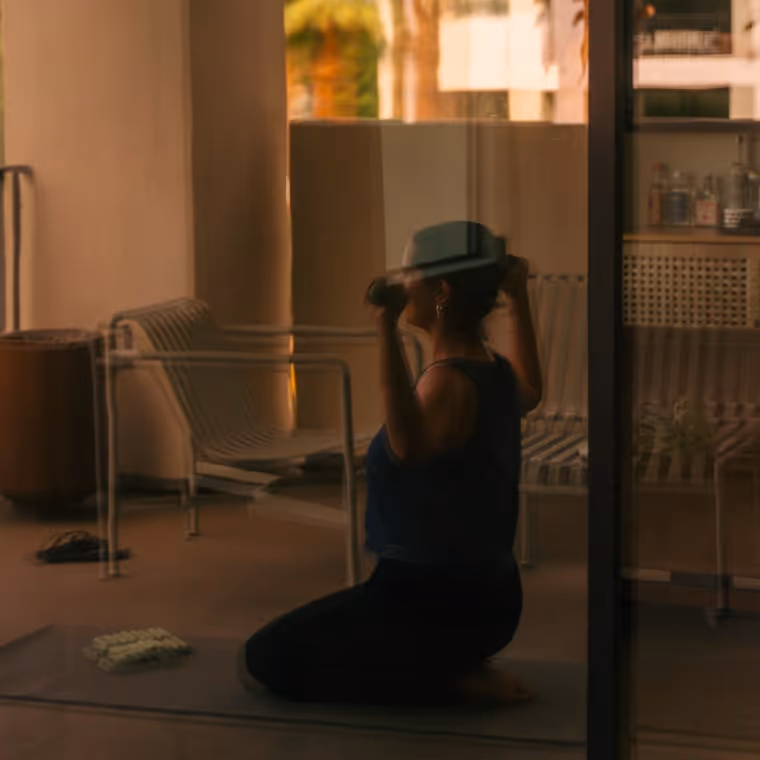 Woman exercising with dumbbells on a hotel balcony, reflected through glass door.