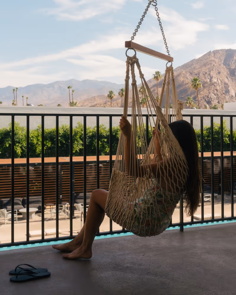 Guest relaxing in a hammock chair on balcony with mountain and palm tree views.