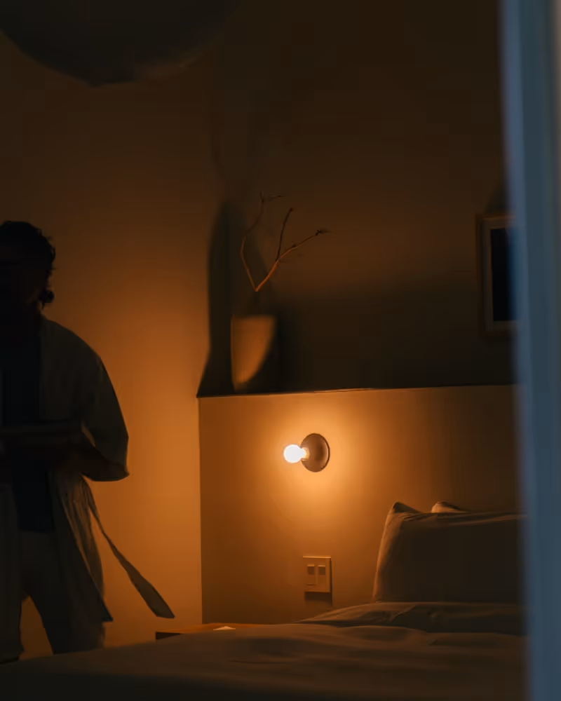 Dimly lit hotel bedroom with glowing wall light and minimal modern decor.