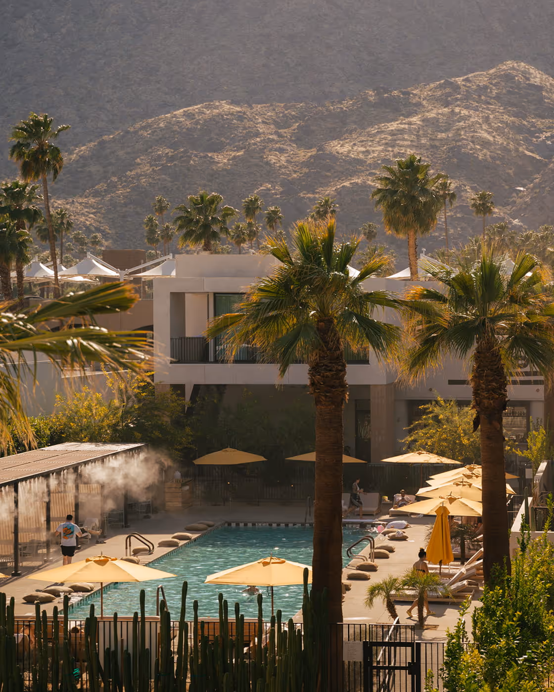 Resort pool surrounded by palm trees, yellow umbrellas.