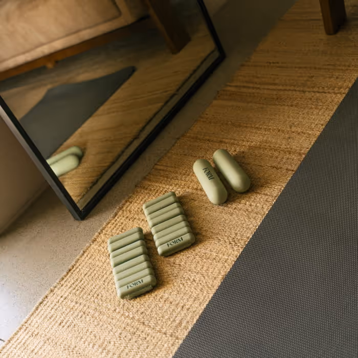 Set of sleek green FORM fitness weights and exercise accessories placed on a woven mat next to a mirror.