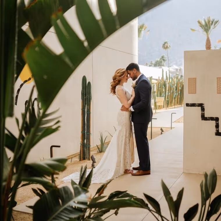 Bride and groom sharing intimate moment at modern desert wedding venue with cacti and palm trees in background