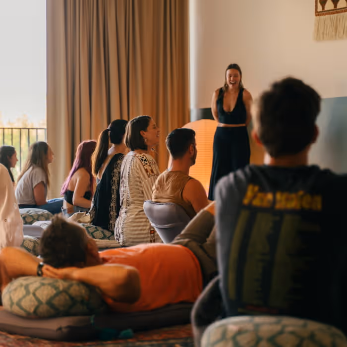 Wellness retreat group session with participants seated on cushions listening to instructor in cozy bohemian-style room