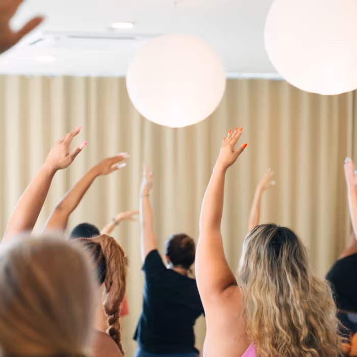 Group fitness class participants with raised arms during yoga or dance workout in bright studio with paper lanterns