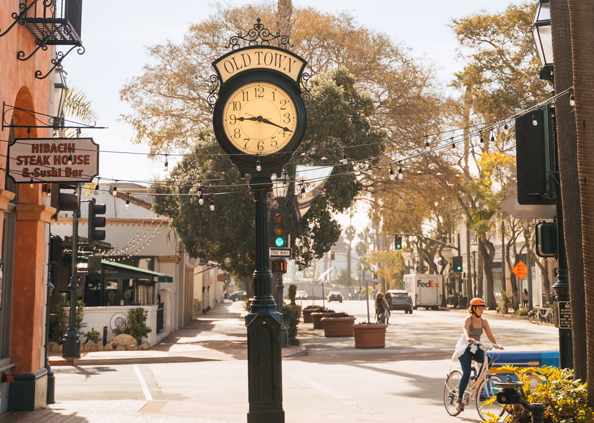 Old Town vintage street clock on ornate post with cyclist passing by, Hibachi Steak House sign, sunny downtown street