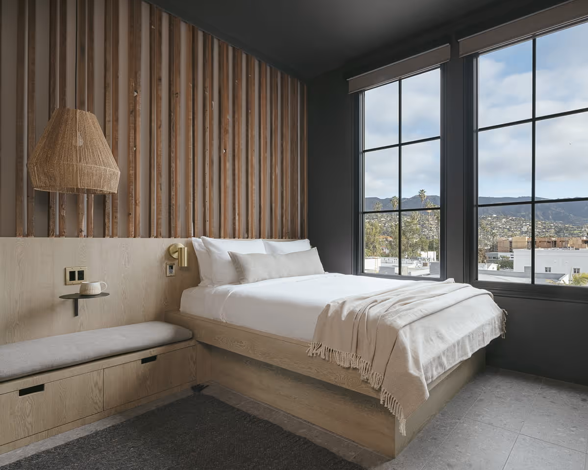 Contemporary hotel bedroom featuring vertical wood slat headboard wall, platform bed with white linens, and mountain city