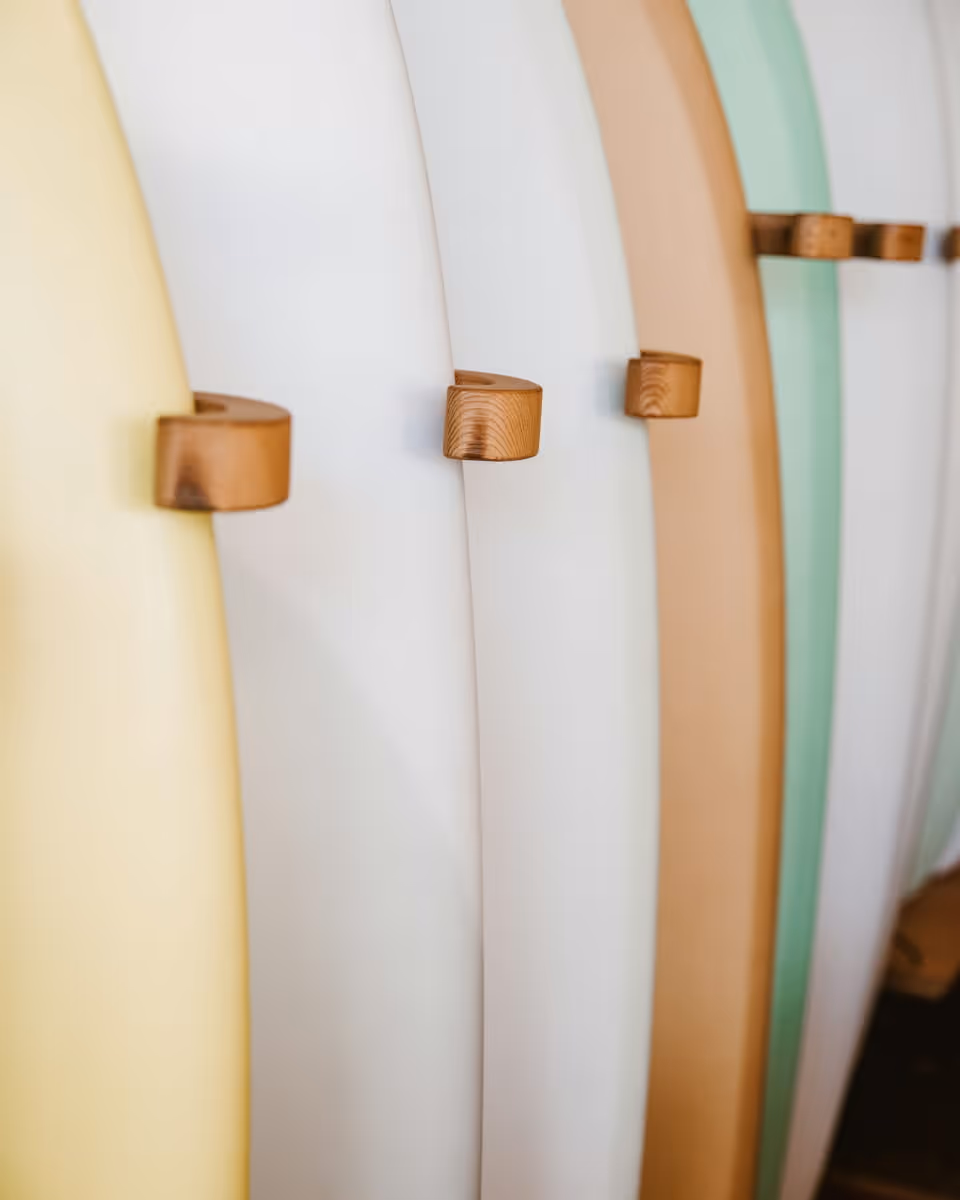 Colorful surfboards in pastel yellow, white, tan, and mint green displayed on wooden wall-mounted rack in surf shop