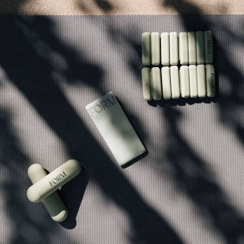Overhead view of FORM workout accessories including sage green dumbbells, resistance band, and adjustable wrist weights on