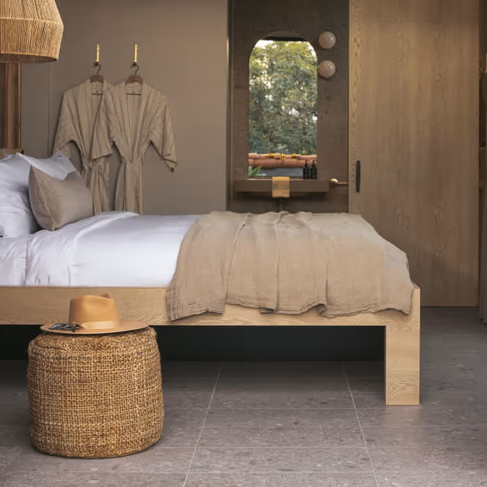 Modern boutique hotel bedroom with oak platform bed, linen bedding, woven pouf, bathrobes, and earth-tone neutral decor