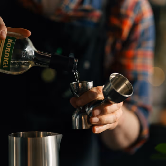 Bartender pouring Bordiga vermouth into jigger while preparing craft cocktail with stainless steel shaker in background
