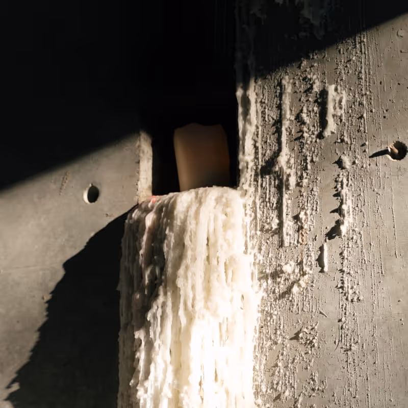Melted white candle wax dripping down weathered concrete wall in dramatic natural lighting with dark shadows