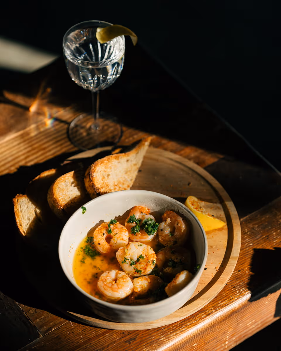 Gambas al ajillo garlic shrimp in butter sauce with toasted bread and martini cocktail on wooden serving board