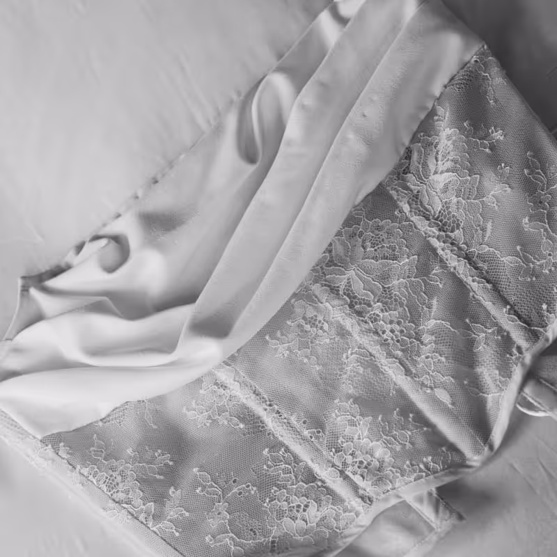 Elegant white bridal corset with delicate floral lace detailing laid on satin fabric, wedding day details