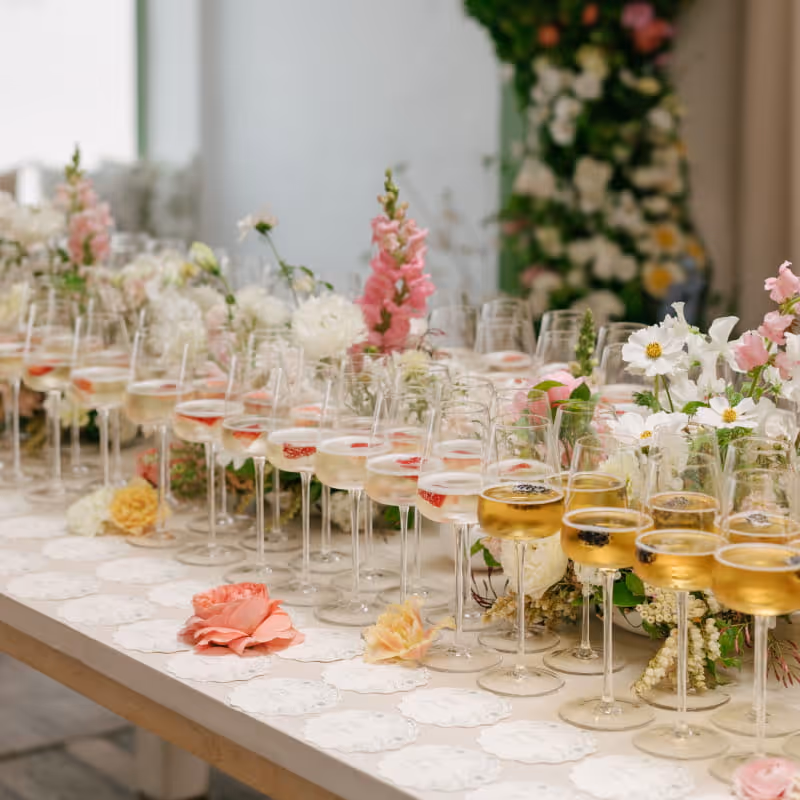 Champagne glasses with strawberries and edible flowers arranged on decorated table with pink and white floral arrangements