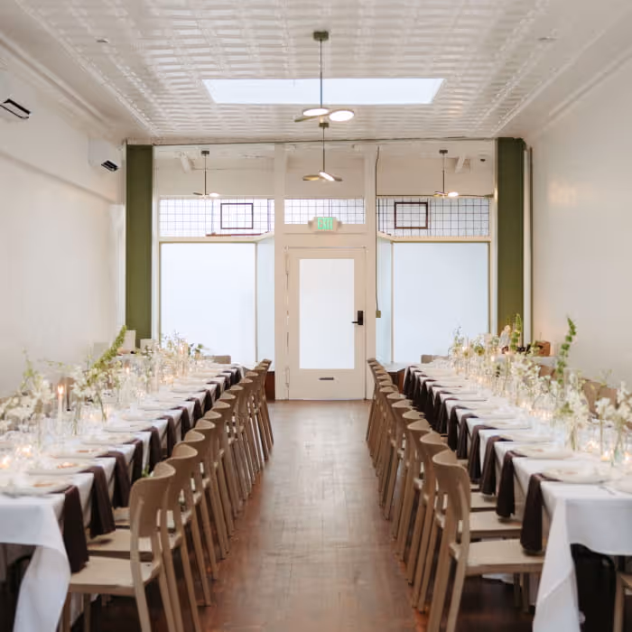 Elegant wedding reception venue with long banquet tables, white linens, floral centerpieces, and modern minimalist decor
