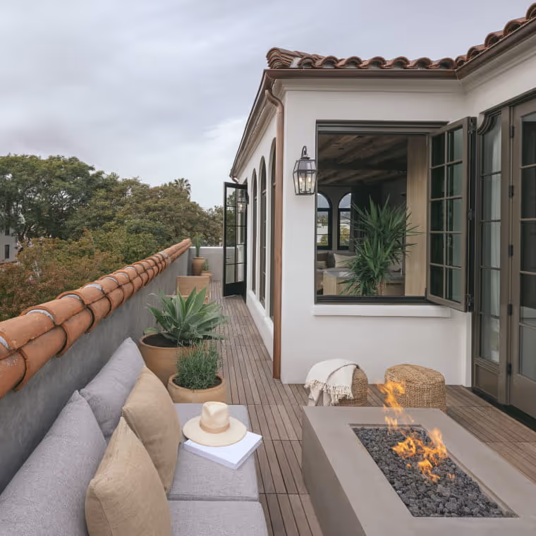 Spanish-style rooftop terrace with modern fire pit, L-shaped outdoor sofa, terracotta tiles, and potted succulents
