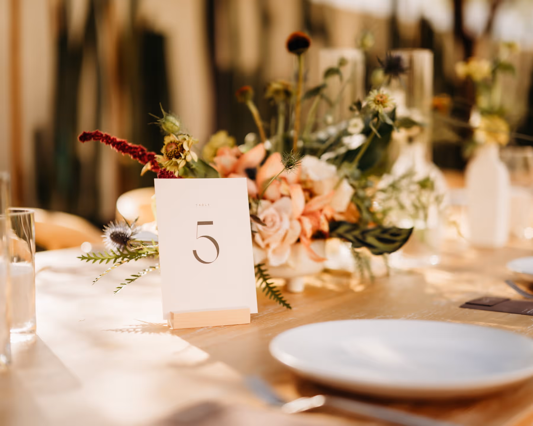Outdoor wedding table decorated with white floral arrangements, candles, and wooden chairs against cactus backdrop