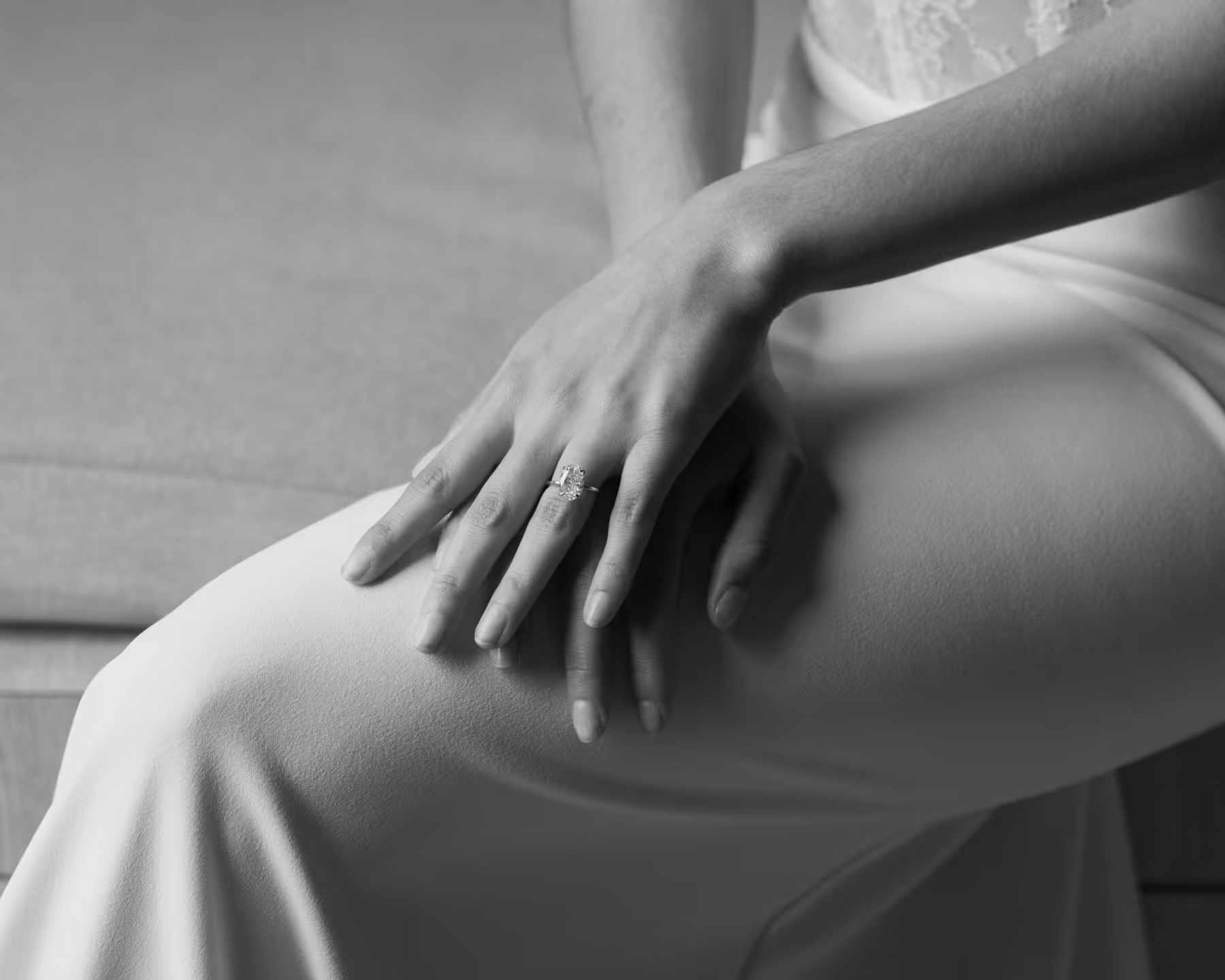 Black and white close-up of a bride's hands resting on her silk wedding dress, showcasing her diamond engagement ring.