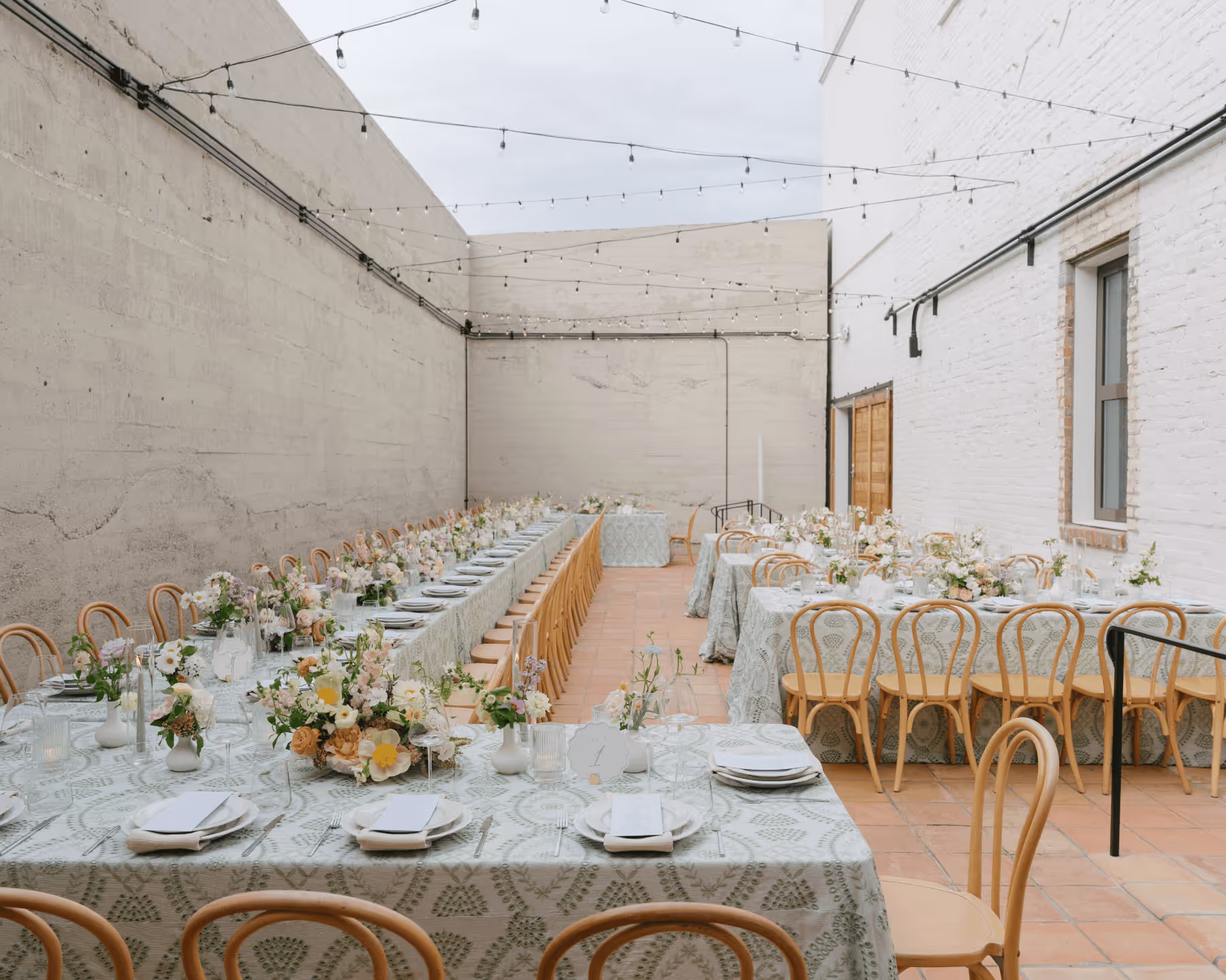 Elegant outdoor wedding reception with long tables covered in patterned linens, floral centerpieces, and string lights