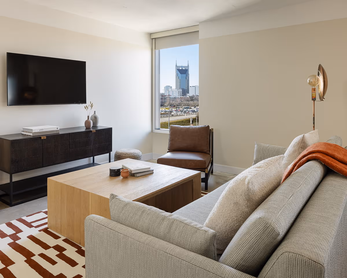 Contemporary living room with gray sectional sofa, wooden coffee table, leather accent chair, and Nashville skyline view