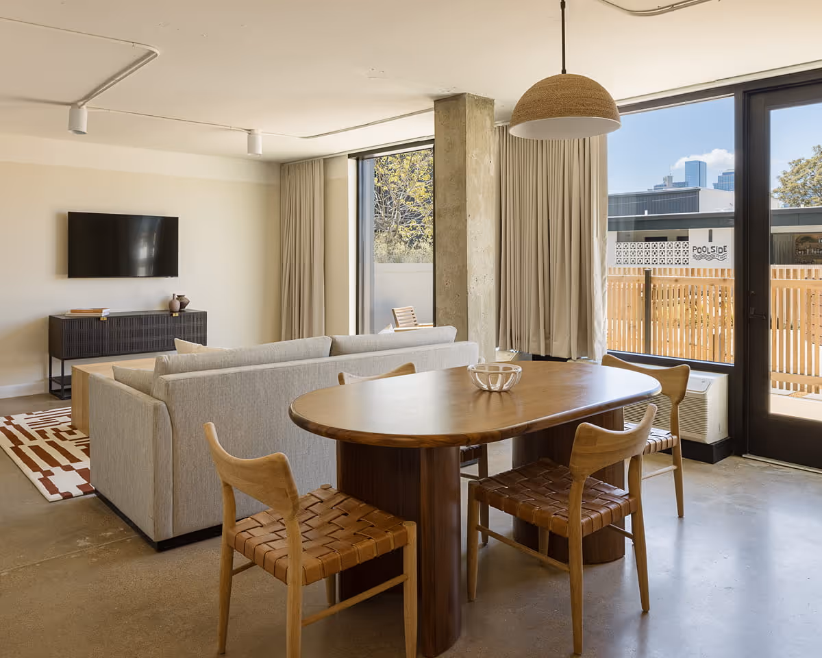 Hotel suite dining and living space featuring oval wooden table with woven leather chairs, sectional sofa, TV console,