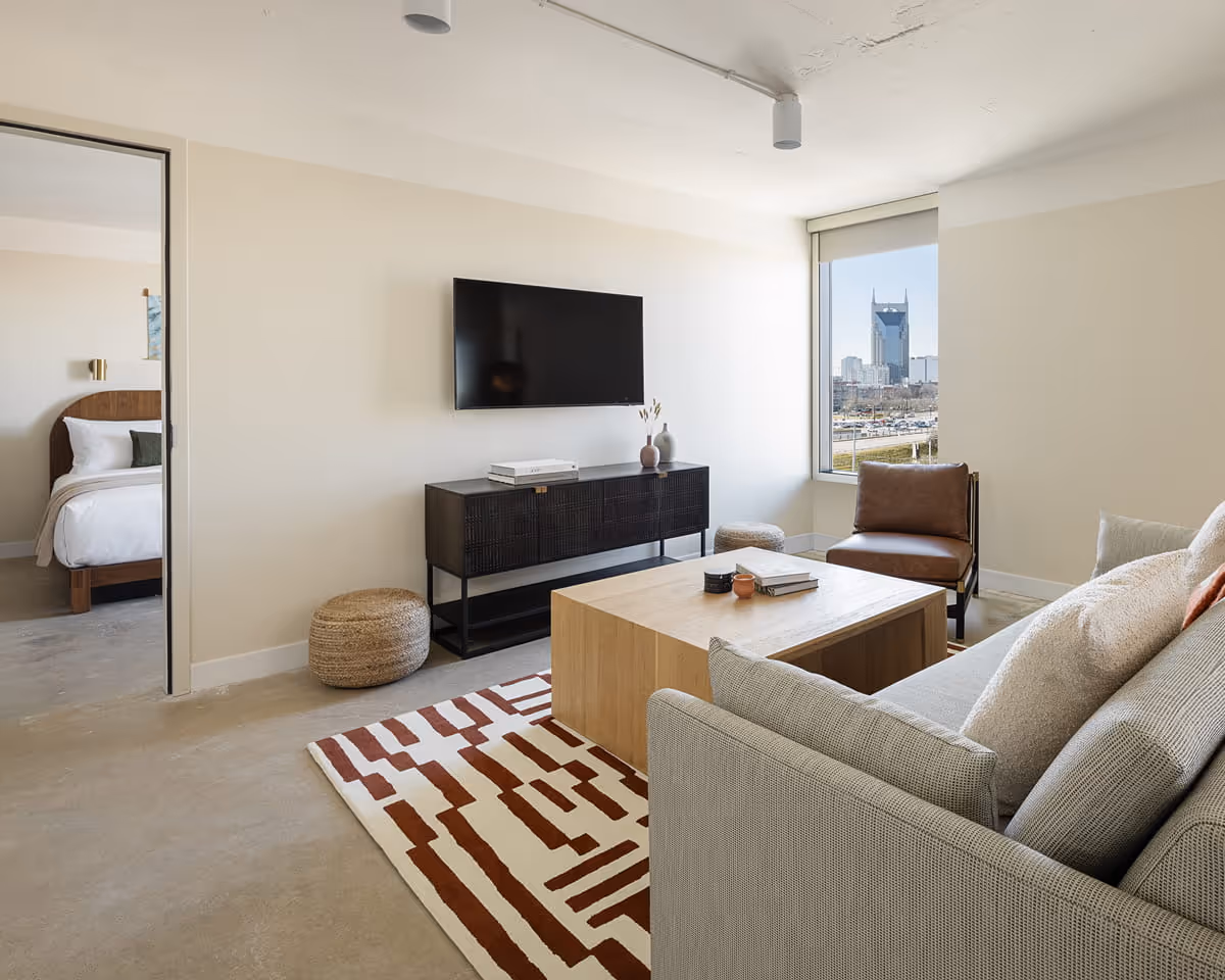 Modern apartment living room with gray sofa, geometric rug, and wood coffee table, featuring Nashville skyline view through