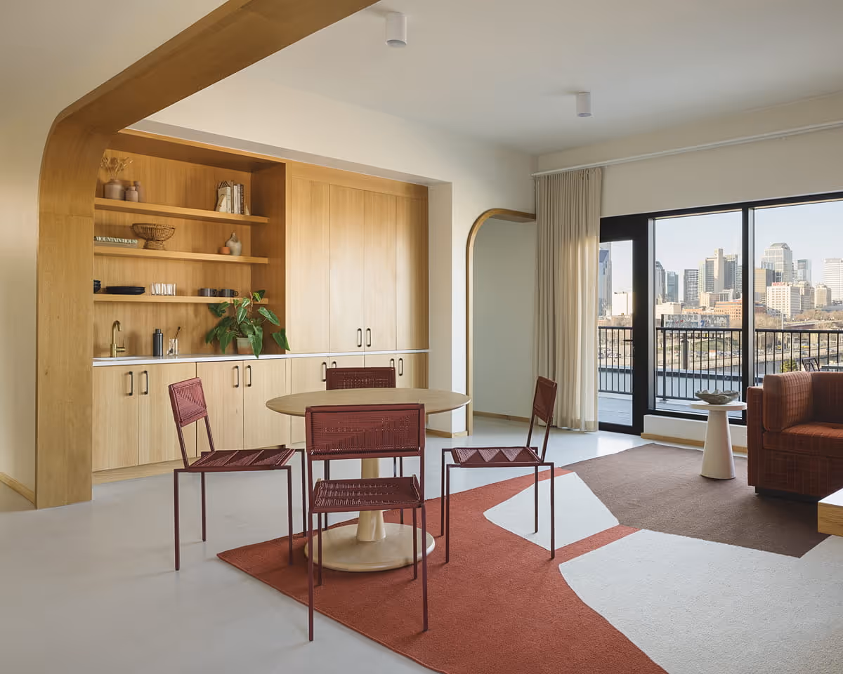 Contemporary hotel suite living area with oak kitchenette, round dining table, burgundy woven chairs, and downtown Nashville