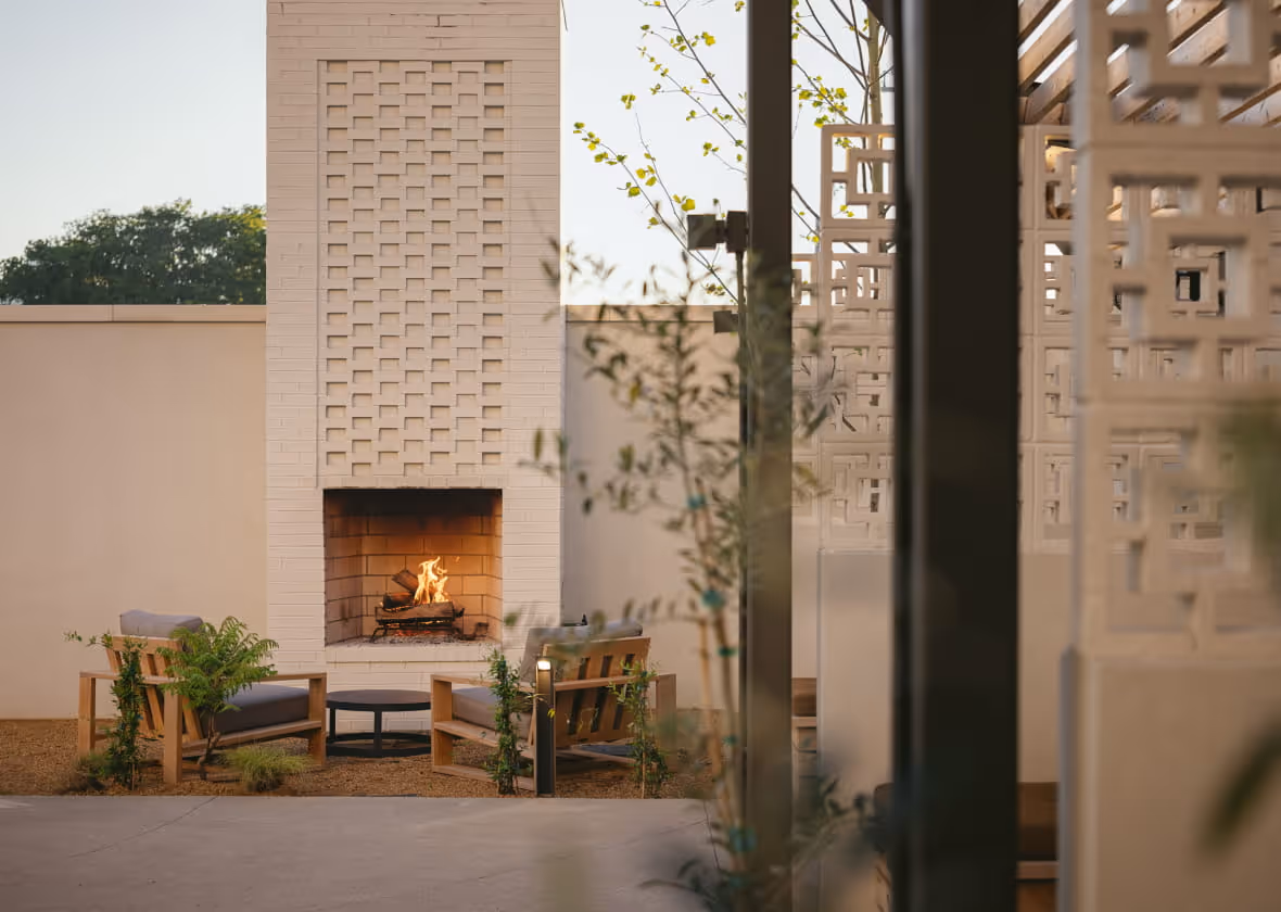 Modern outdoor patio with white brick fireplace, wooden lounge chairs, and decorative concrete block screens at dusk.